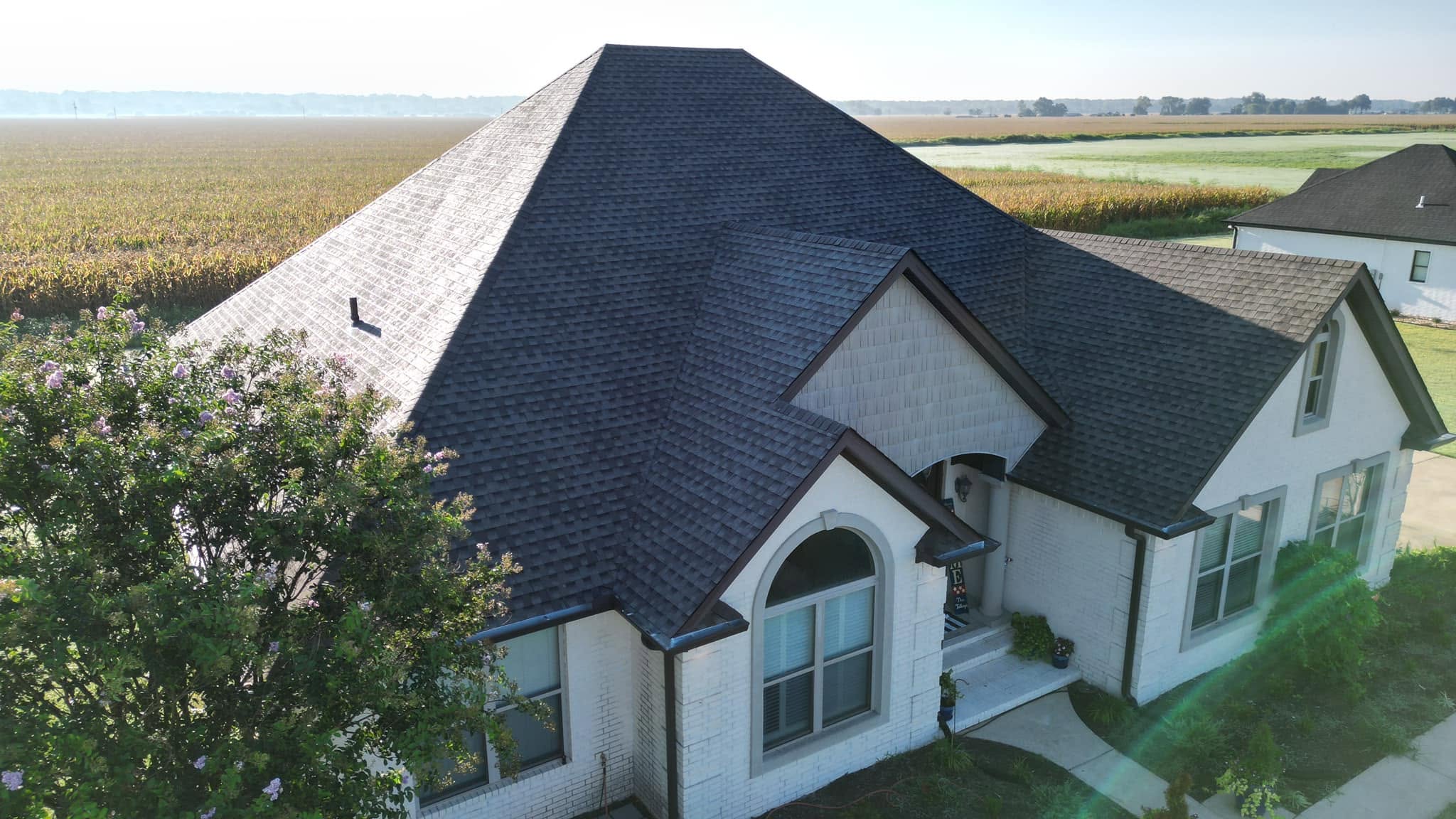 Large hip-roof home with complete roof replacement, farmland in background